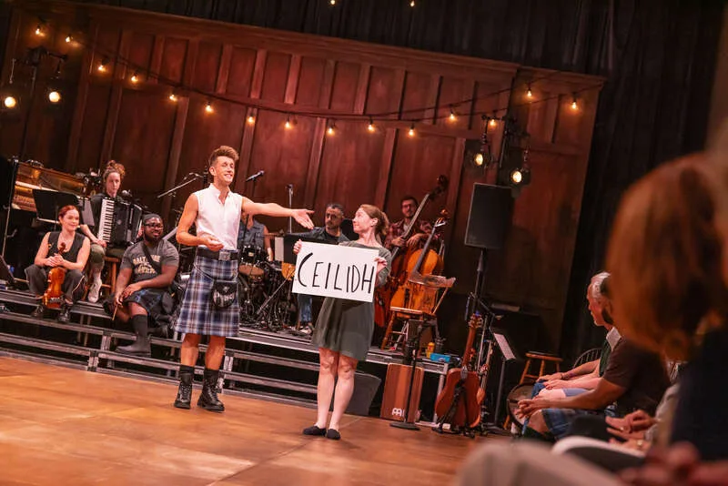 Performers hold a handmade CEILIDH sign beside a live folk band on stage