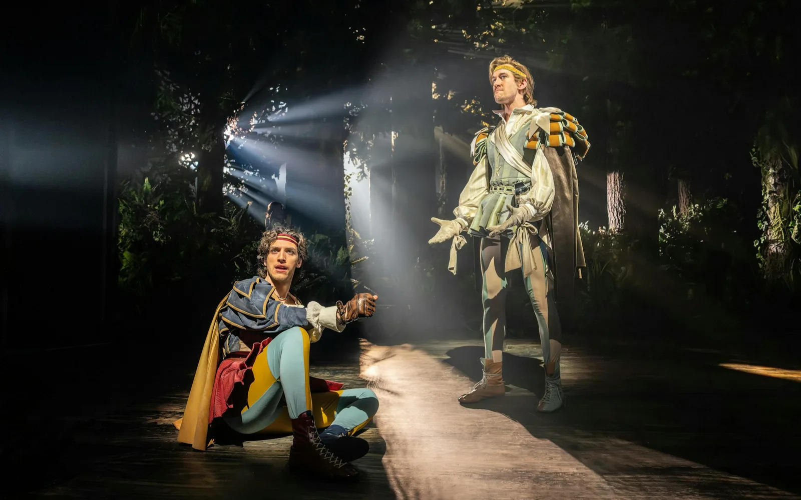 Two princes in extravagant costumes strike dramatic poses in a single shaft of light