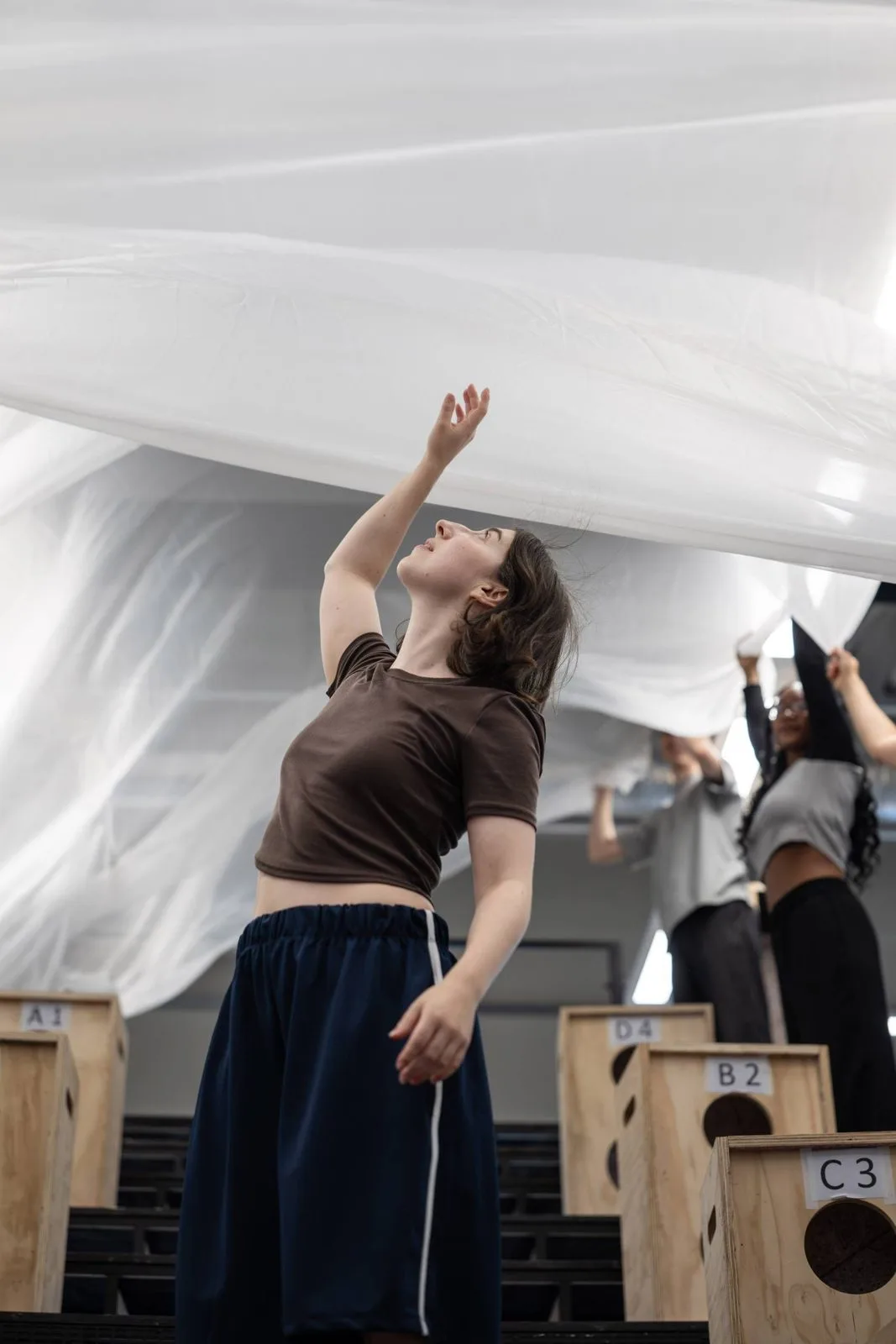 Olivia Marcus in rehearsal for Jane Eyre, reaching up towards a billowing white sheet held above her by members of the company