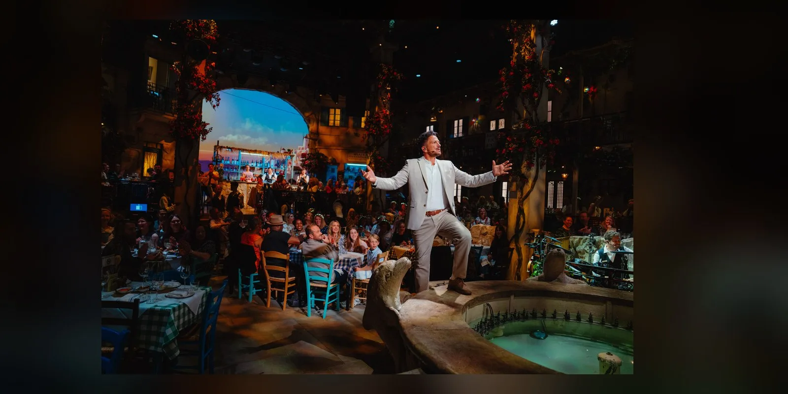 Peter Andre as Nikos, arms outstretched, in the taverna surrounded by diners at The O2