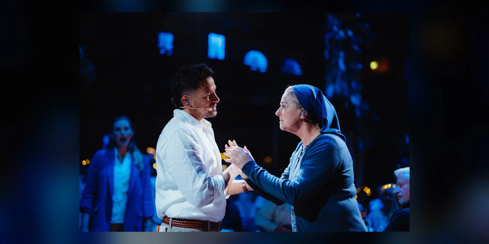 Peter Andre as Nikos holding hands with a performer in a blue headscarf on stage
