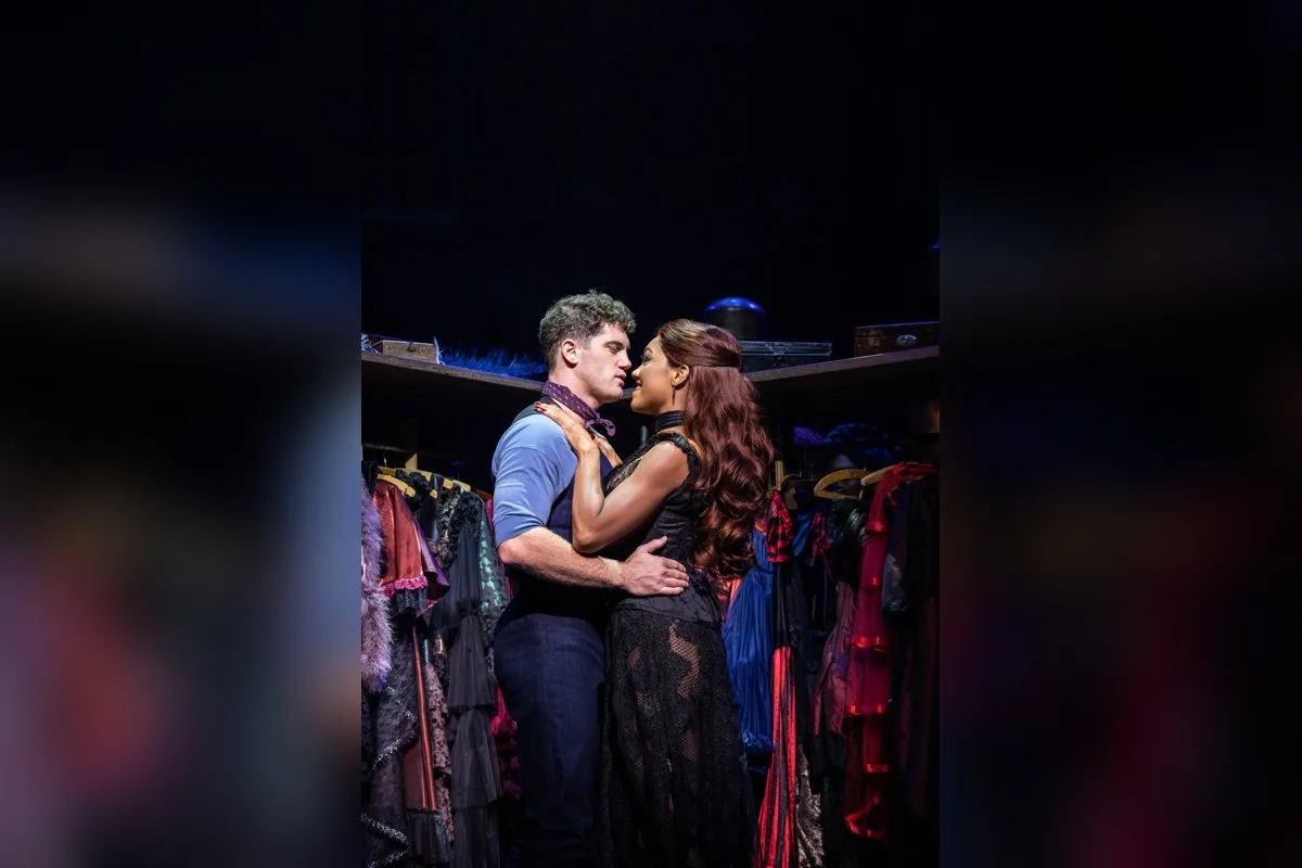 Christian and Satine in a close embrace backstage, surrounded by racks of costumes