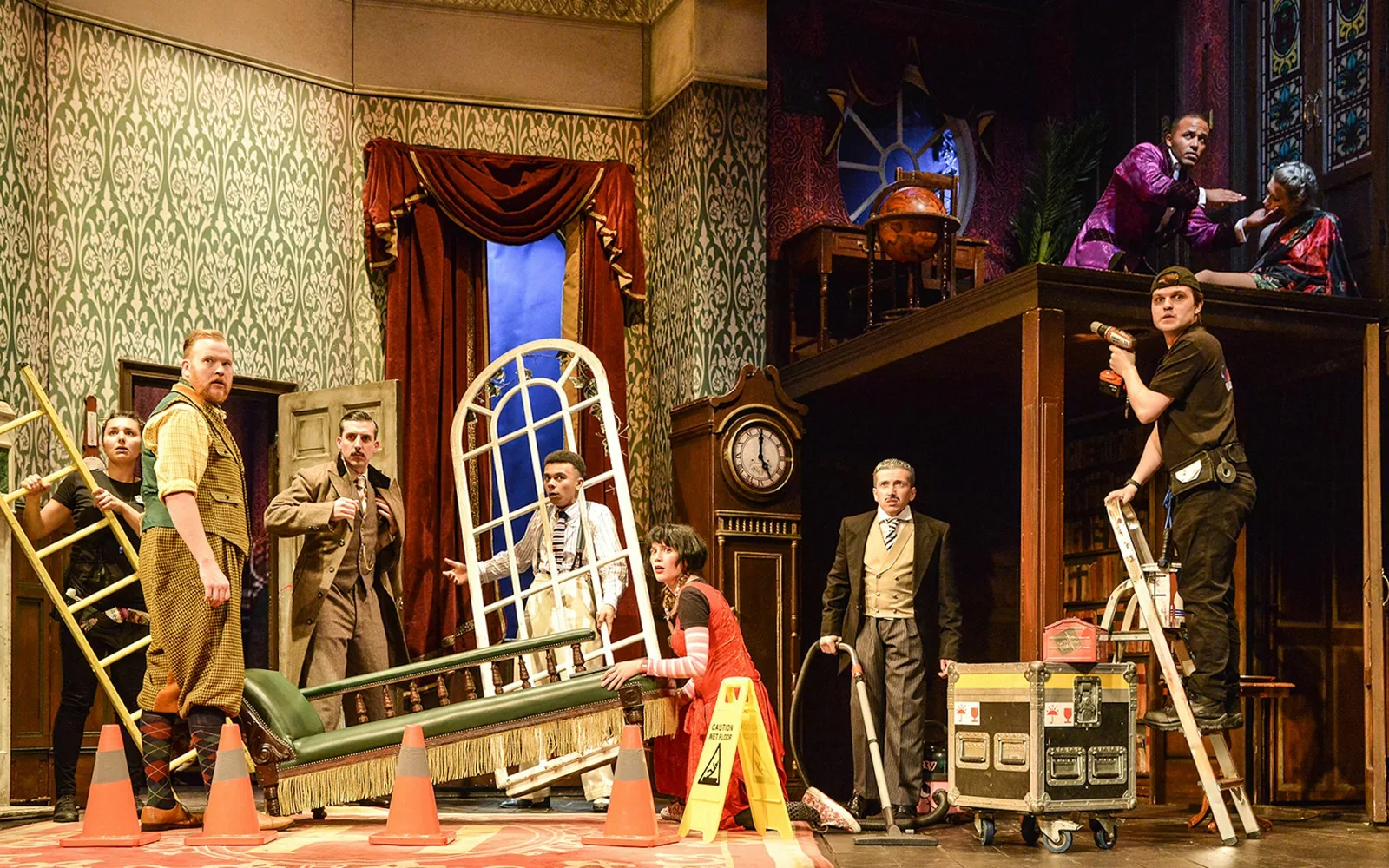 Actors in 1920s costume look around in alarm on a collapsing country-house set strewn with ladders and traffic cones