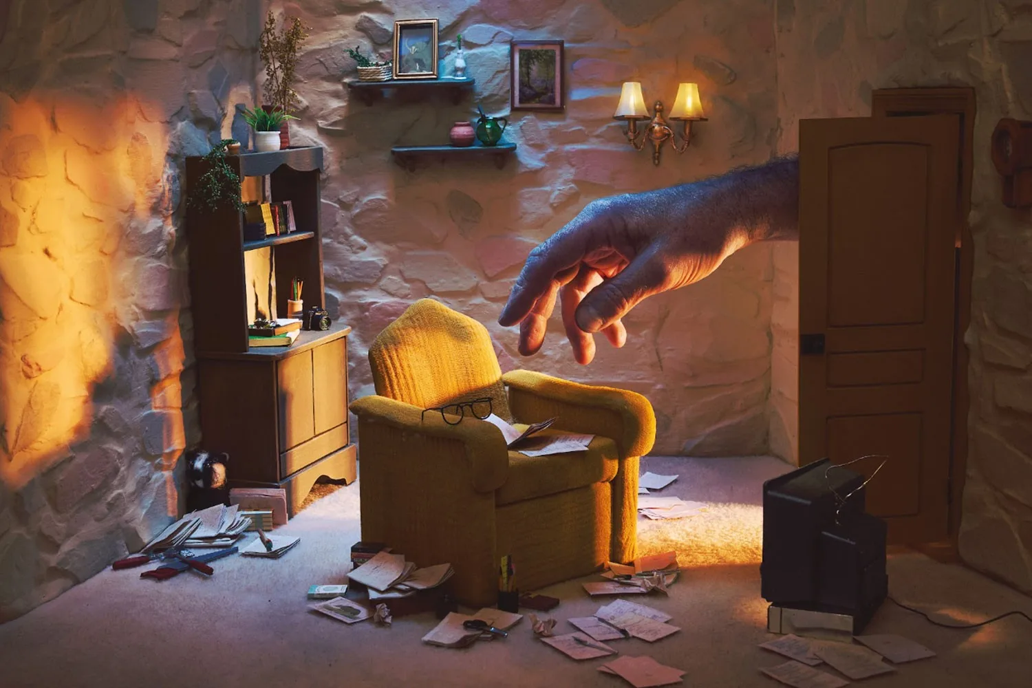 Miniature model living room with a yellow armchair, scattered papers and a giant human hand reaching in through the doorway