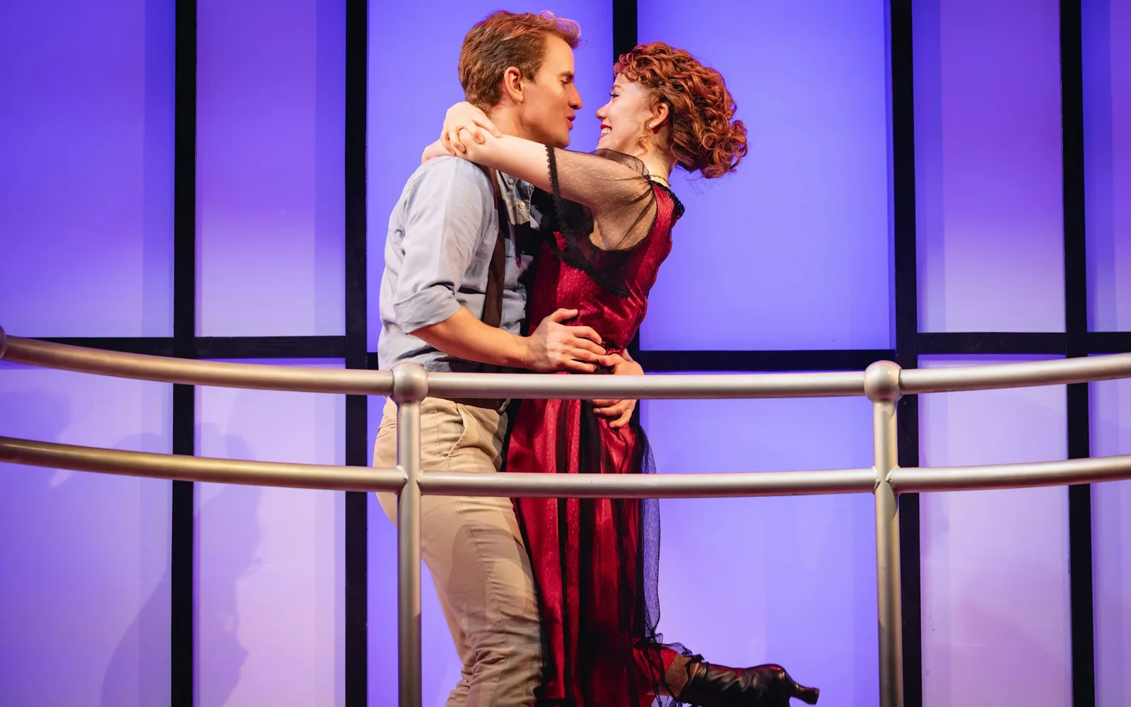Two Titanique performers as Jack and Rose embrace at a ship's railing against a purple backdrop