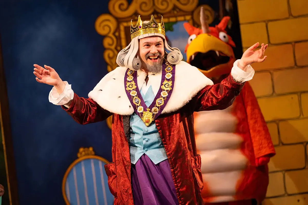 The King in a gold crown, fur-trimmed red robe and chain of office beams at the audience, with Zog behind him, in Zog and the Flying Doctors
