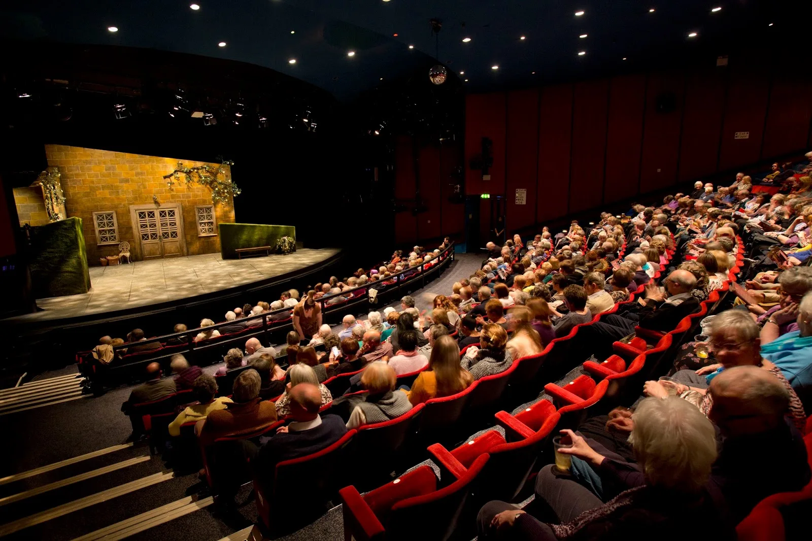 A full auditorium of red seats facing the stage at Queen's Theatre Hornchurch