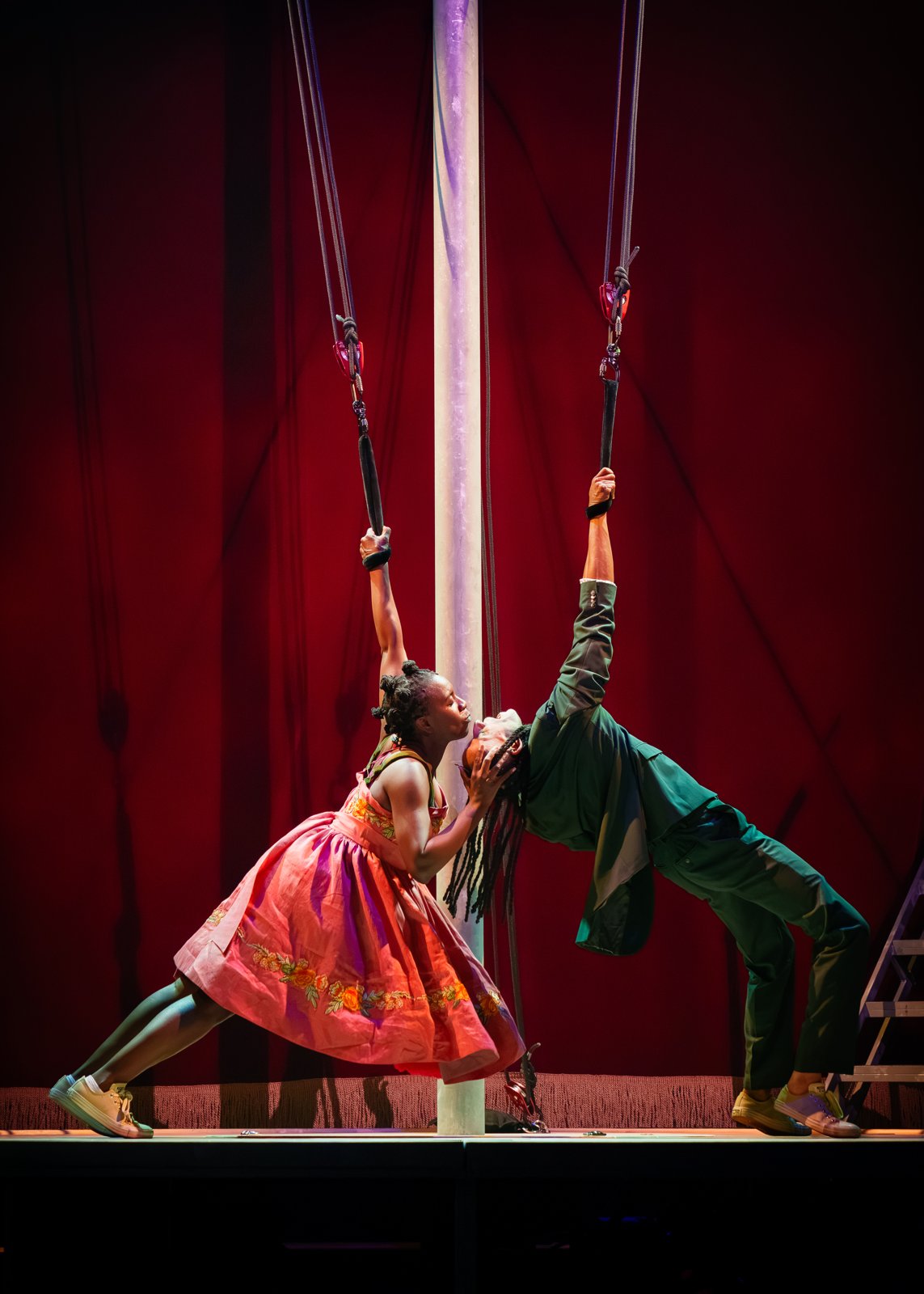 Nandi Bhebhe as Yseult and John Leader as Tristan leaning into a kiss as they hang from ropes on either side of a pole in Tristan & Yseult. Photo: Steve Tanner